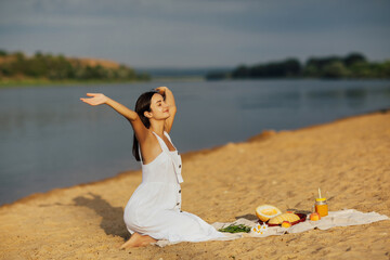 Wall Mural - Summer vacation at the beach. Young pretty woman holding hands up and smiling happy. Picnic on the sandy beach. Freedom and nature concept. Copy space.