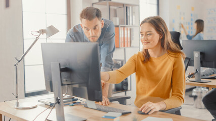 Female Specialist Works on Desktop Computer, Project Manager Stands Beside and gives Advice on Optimizing Workflow for Customer Experience Management. Modern Office with Diverse Team of Professionals