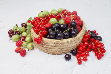 Wall Mural - Bright variety of berries lie in a wicker basket on a white background. A mix of vitamins from summer healthy food.