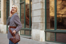 Street Fashion Portrait Of Happy Smiling  Woman Wearing Trendy Checkered Blazer, Wide Belt, Holding Brown Leather Handbag. Model Posing In Street Of European City. Copy, Empty Space For Text
