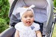 © Any Grant - a small child a girl of 7 months sits in a stroller in the summer in a white dress and shows her tongue