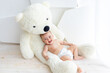 © Any Grant - A small child a girl 6 months old is lying on a large soft bear in a bright apartment in diapers