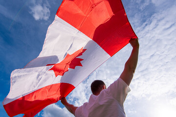 Man holding The National Flag of Canada against blue sky