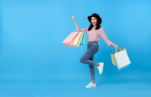 Happy Young Thai Asian Female Carrying With Both Arms Raised In A Ecstatic Gesture And Shopping Bags On Blue Copy Space Background.