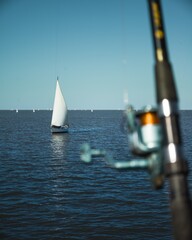 Sticker - Vertical shot of sailboats in a calm sea with a blurred fishing pole in the foreground