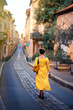 Vertical picture of old narrow stone street of Aix-en-Provence, France with back of walking away faceless tourist woman in yellow dress with yellow bag. Travel tourism destination Provence