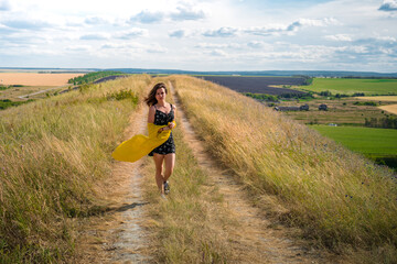 A girl in a dress and a yellow scarf fluttering in the wind poses against the backdrop of a picturesque mountain nature with a lake