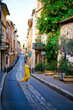 Vertical picture of old narrow stone street of Aix-en-Provence, France with smiling tourist woman in yellow dress with yellow bag. Travel tourism destination Provence