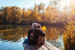 © maryviolet - Senior family couple relaxing by autumn lake. Man and woman enjoying nature and hugging sitting on pier