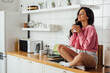 © LIGHTFIELD STUDIOS - Beautiful woman holding cup of coffee while sitting with closed eyes on kitchen worktop
