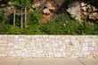 Garten und Landschaftsbau: Terrassenförmige Gestaltung eines felsigen Hanggrundstücks mit Mauern aus Natursteinen und mit Grünpflanzen, Stauden und Efeu umgeben von Schotter bepflanzt