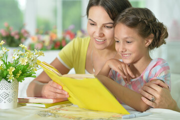 Poster - Cute girl reading book with mother at the table at home