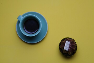 Poster - High angle closeup shot of a chocolate cupcake and a cup of coffee on a yellow surface