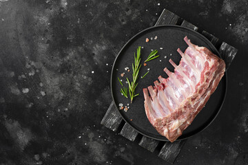 Wall Mural - Raw ribs of a young lamb. Raw lamb ribs in a black ceramic plate on the black kitchen table. Raw meat of a young lamb on the table