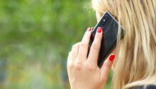 Blonde Girl Talking On The Phone, Red Manicure, Long Hair, Black Phone. Close-up, Blurred Green Background. Life Style.