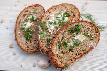 Wall Mural - Fresh soft pieces of wholegrain bread with seeds with butter, dill, salt and garlic on a white wooden background. Top view.