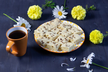 Cookies with seeds on plate on black wooden table with yellow and white flowers, cup of coffee