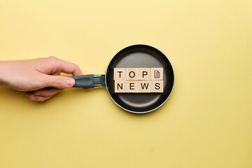 Top news concept on a frying pan on a yellow background.
