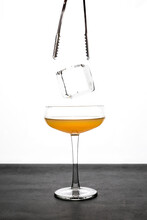 A Big Ice Cube Falling Into A Coupe Glass With Orange Cocktail