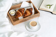 © gorina_anna - Breakfast in bed with two croissants and butter on the wooden tray, a cup of coffee and open book on the white sheet with blanket. Slow life.
