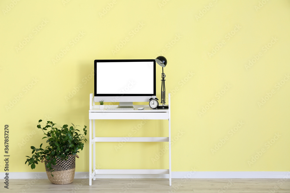 Modern PC monitor on table near color wall