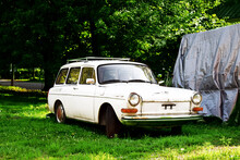 An Old Vintage Car In A Grass Field With Trees In Background.  Antique White Station Wagon. Summer Day With Sun And Shade. 