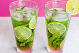 Fototapeta Las - Non-alcoholic cold mojito in two glass glasses. Lemonade with lime and mint on a light background