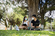© Fernanda - Young Hispanic couple in the park with disposable face masks - young people studying with an electronic tablet and a book in a natural park - social distancing - general shot