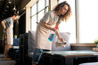 © pressmaster - Young curly-haired waitress in apron spraying detergent while bussing tables in cafe before opening