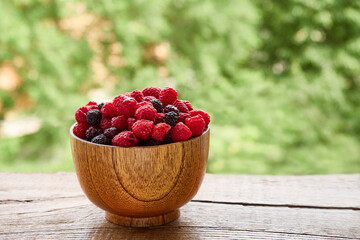 Wall Mural - Wooden bowl of delicious red and black raspberries on a background of green foliage