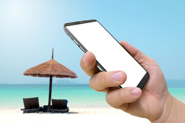 Wall Mural - side view of hand hold mobile phone and blank display with blurred tropical beach for traveling, advertising concept concept