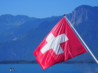 Red and white Swiss national flag on landscapes at Lake Geneva in european Montreux city in canton Vaud in Switzerland, clear blue sky in 2017 warm sunny summer day on July.