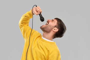 Wall Mural - music and people concept - young man in yellow sweatshirt with microphone singing over grey background
