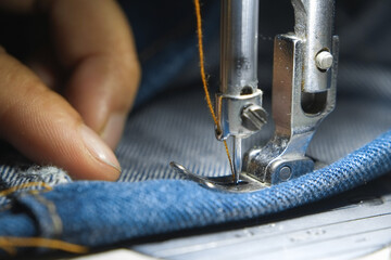 Wall Mural - Macro shoot hand of the seamstress is using industrial sewing machine to sew the seams of blue jeans close-up.