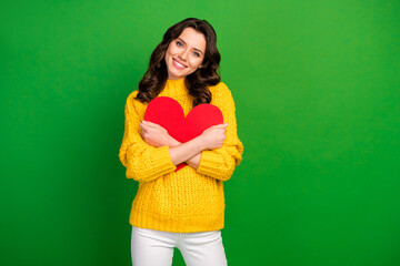 Wall Mural - Photo of charming toothy lady hold red big paper heart close to chest lovers day romantic mood wear knitted yellow pullover white trousers isolated bright green color background