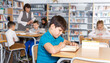 © JackF - Focused boy reading in school library on background with other students and teacher
