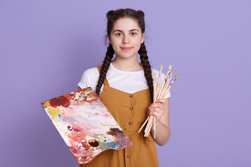 Talented woman creating beautiful watercolor floral design, standing isolated over lilac background, looking directly at camera, wearing casual attire.