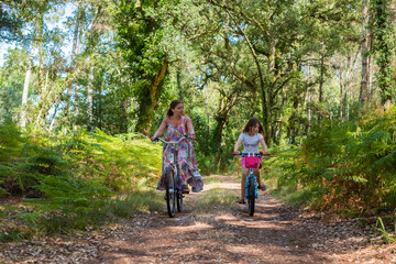 Wall Mural - cute little girl and her mom riding a bicycle in a cork oak forest