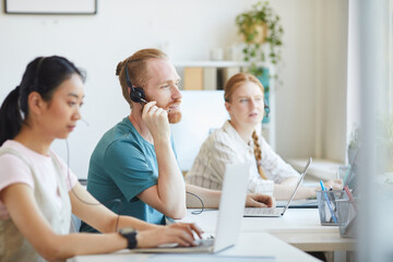 Wall Mural - Group of people working in call center they wearing headphones sitting at the table and consulting clients