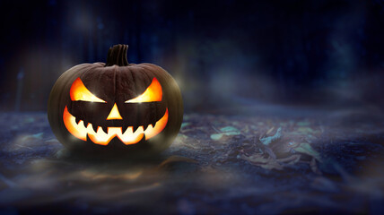 One spooky halloween pumpkin, Jack O Lantern, with evil face and glowing eyes on a leaf covered forest floor at night.