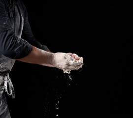 Wall Mural - baker in black clothes holds white wheat flour in palms on black background