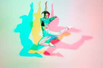 Wall Mural - Young beautiful woman dancing hip-hop, street style isolated on studio background in colorful neon light. Fashion and motion, youth, music, action concept. Trendy clothes. Copyspace for ad.