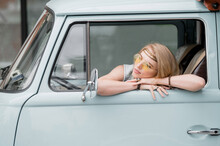 A Beautiful Young Hippie Woman In Yellow Sunglasses Looks Out The Window Of A Blue Vintage Minivan. Make Love, Not War. Girl Child Flowers Driving In A Retro Van. Auto Travel Concept.