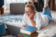 © Georgii - Cute teen girl student in casual clothes, glasses lying on floor at laptop with books. Back to school. Exam preparation