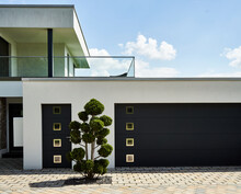 Entrance And Garage Of A House In Minimalist Design, With An Unnaturally Trimmed Tree