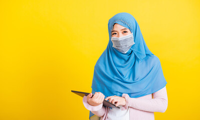 Wall Mural - Asian Muslim Arab, Portrait of happy beautiful young woman Islam religious wear veil hijab and face mask protect she quarantines disease coronavirus touch on tablet screen isolated yellow background