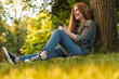© Drobot Dean - Young blonde woman using smartphone under tree in park