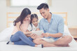 © ChompopsonG - Happy family in the bedroom,Asian father and mother watching cartoon with daughter on smart tablet together at home.Photo series of family, kids and happy people concept.