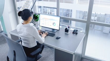 In Open Space Office Businesswoman Working on Her Personal computer with Financial Data, Graphs and Statistics. Shot in Big Bright Modern Open Space Office.