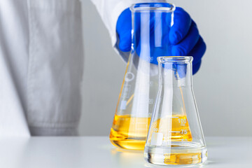 Scientist or doctor in blue gloves pouring some yellow liquid into a flask